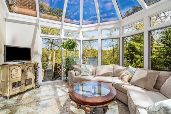 A conservatory with a sofa, TV, and decorative cabinet. - Swan Dive - Waterfront Retreat in Cataumet RPLO032 (Bourne)