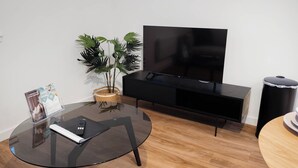 Ein modernes Wohnzimmer mit einem Glastisch, einem Flachbildfernseher, einer schwarzen Unterhaltungseinheit, einer Topfpflanze und einem Mülleimer.