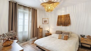 Een slaapkamer met een bed, nachtkastjes, een hanglamp en een raam met gordijnen.