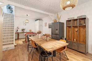 Ein Essbereich mit Holztisch, Stühlen, einem Kühlschrank und einer Schrank mit offenen Regalen.