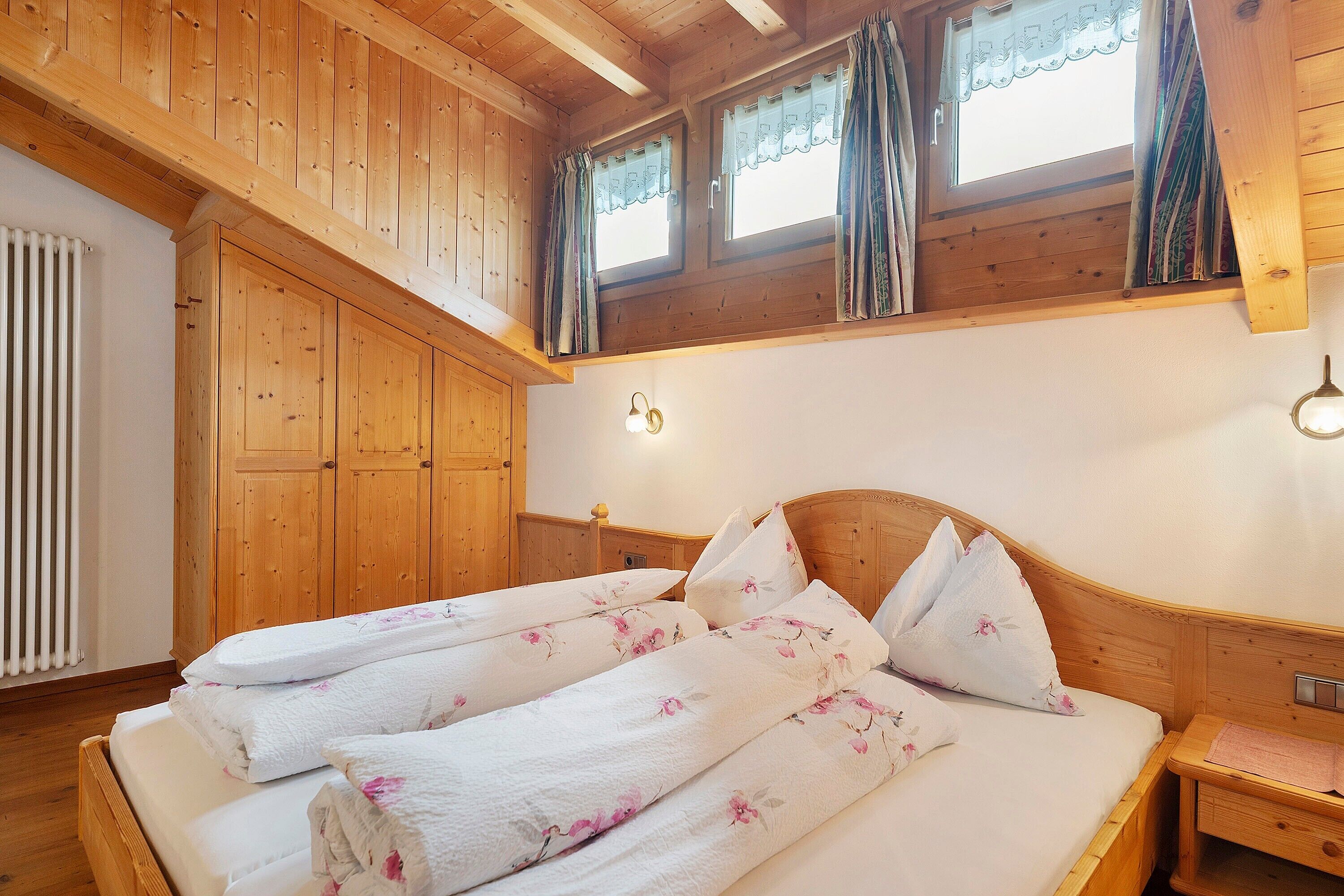 A wooden-paneled room with a bed, a wooden wardrobe, and a window with curtains.