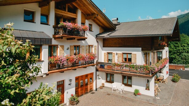 A two-story building with wooden balconies, a covered patio, and a mountain backdrop.