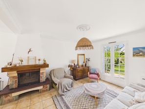 Ein Wohnzimmer mit Kamin, einer Couch, einem Sessel, einem kleinen Tisch und Blick durch eine Glastür.