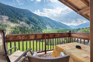 A balcony with a wooden railing, a table with a yellow tablecloth, and a view of a mountainous landscape. - Apartment Margerite 21 with Mountain View and Wi-Fi (Santa Valburga)