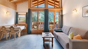 A spacious living area with a wooden ceiling, a dining table with chairs, a sofa, and a view of the outdoors through large windows. - Apartment Margerite 21 with Mountain View and Wi-Fi (Santa Valburga)