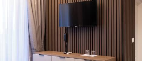 A modern room with a wooden desk, a flat-screen TV mounted on the wall, a mini-fridge, and a red ottoman.