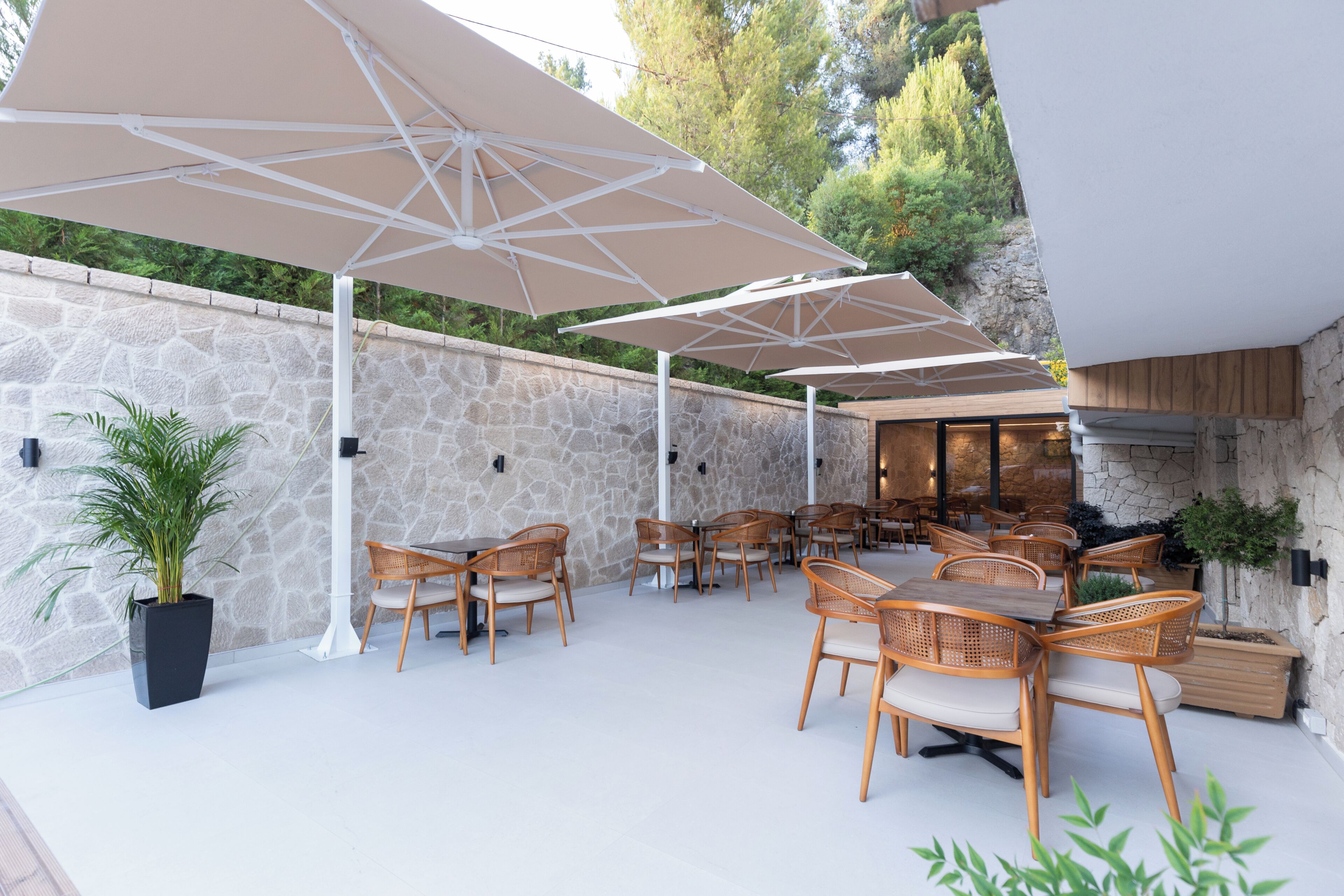 An outdoor patio with stone walls, wooden tables and chairs, and large umbrellas.