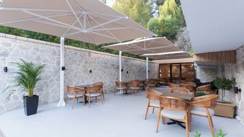 An outdoor patio with stone walls, wooden tables and chairs, and large umbrellas.