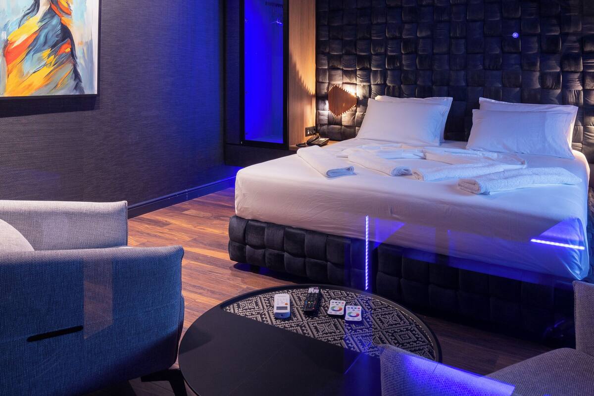 Moderni hotellihuone, jossa on suuri sänky, oleskelualue tuoleineen, pieni pyöreä pöytä ja taulu seinällä.
