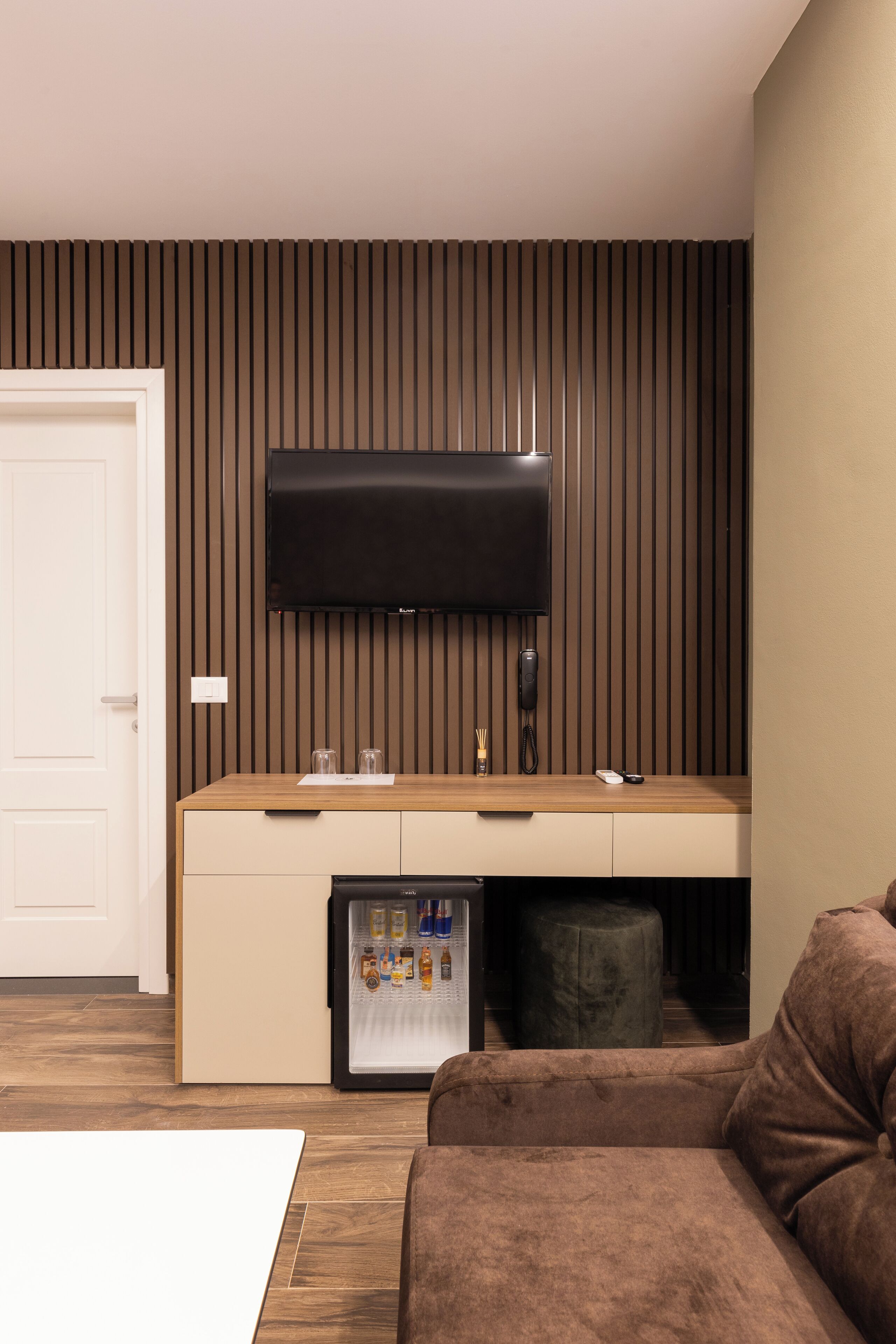 Una sala de estar moderna con un televisor de pantalla plana montado en la pared, un mueble de madera con refrigerador debajo y un sofá marrón.