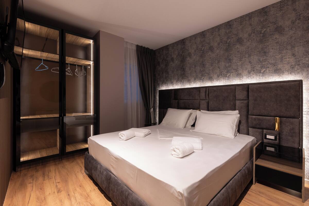 Moderni hotellihuone, jossa on suuri sänky, sisäänrakennettu vaatekaappi ja yöpöytä.
