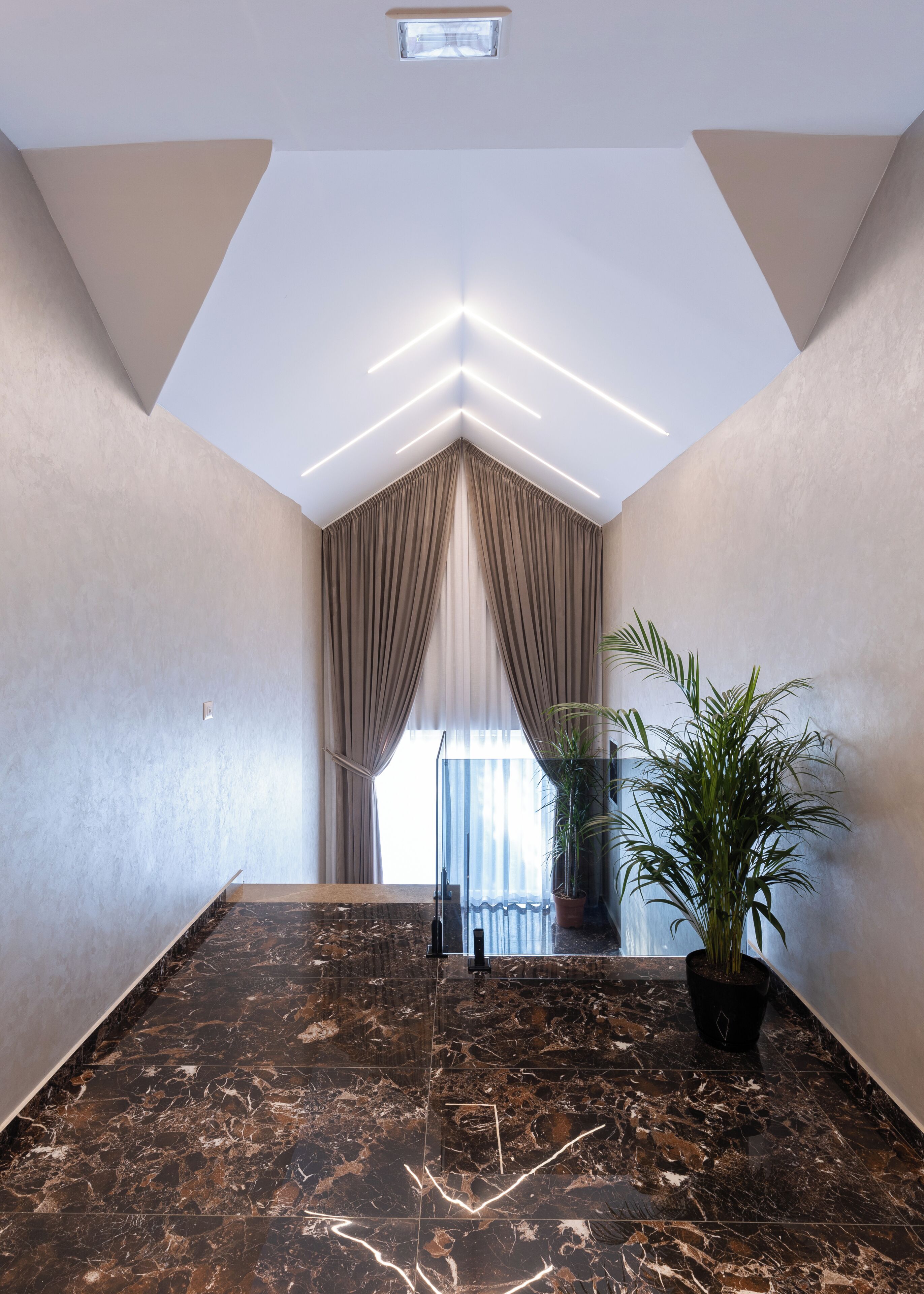 Ein modernes Interieur mit Marmorboden, einer Topfpflanze und Blick durch eine Glastür.