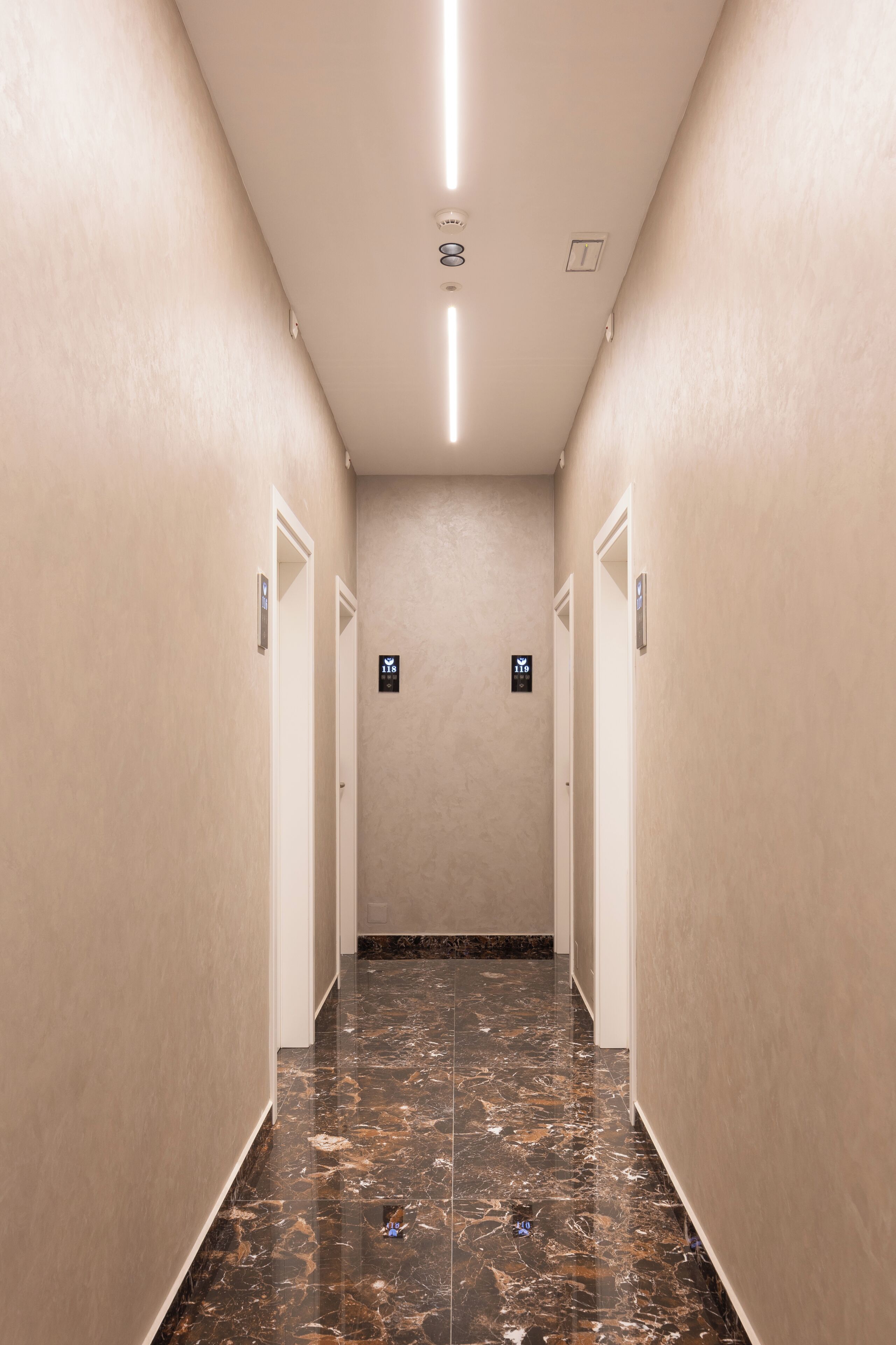 A corridor with marble flooring, beige walls, and doors marked with room numbers.