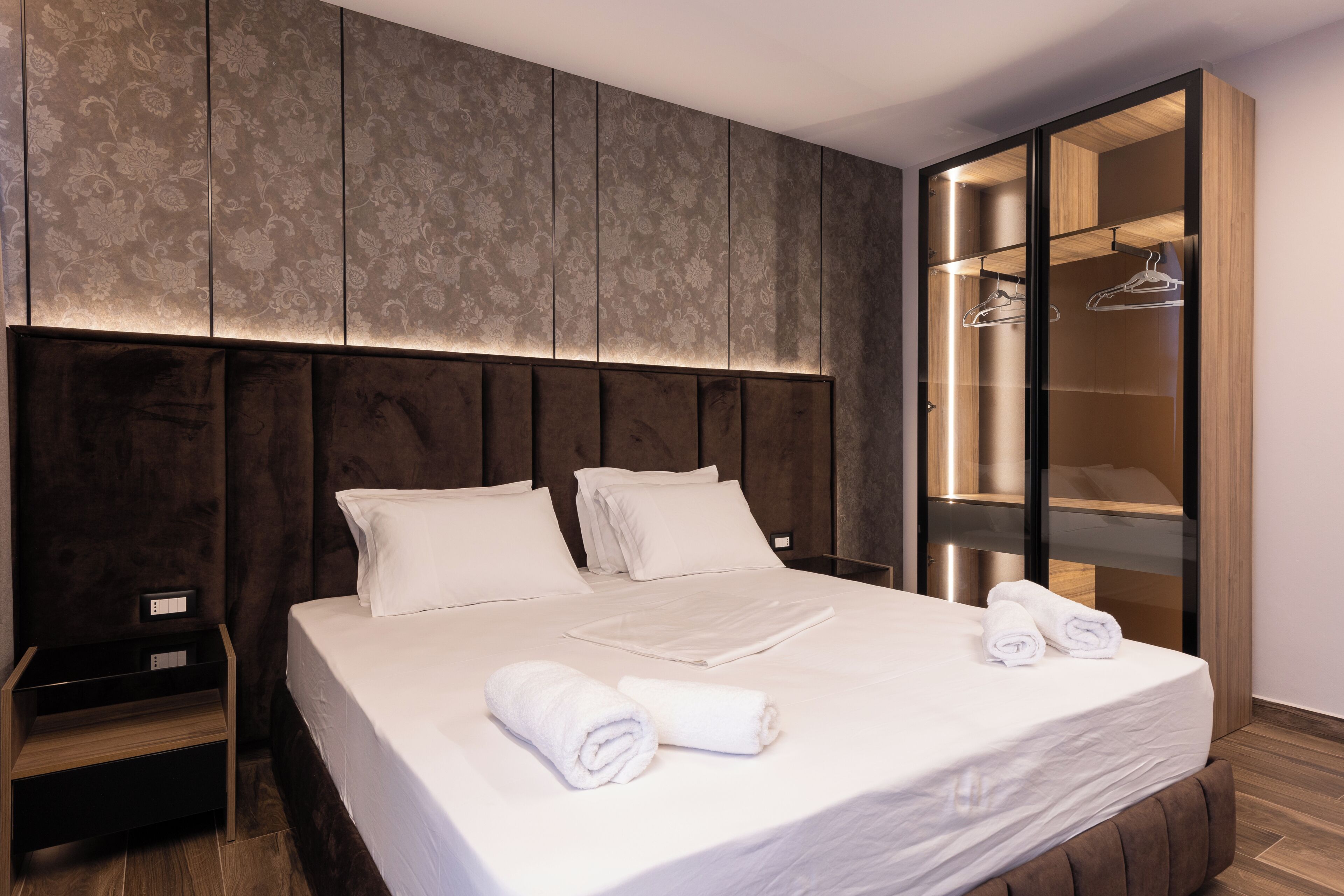 A hotel room with a large bed, a wardrobe with a mirror, and a nightstand.
