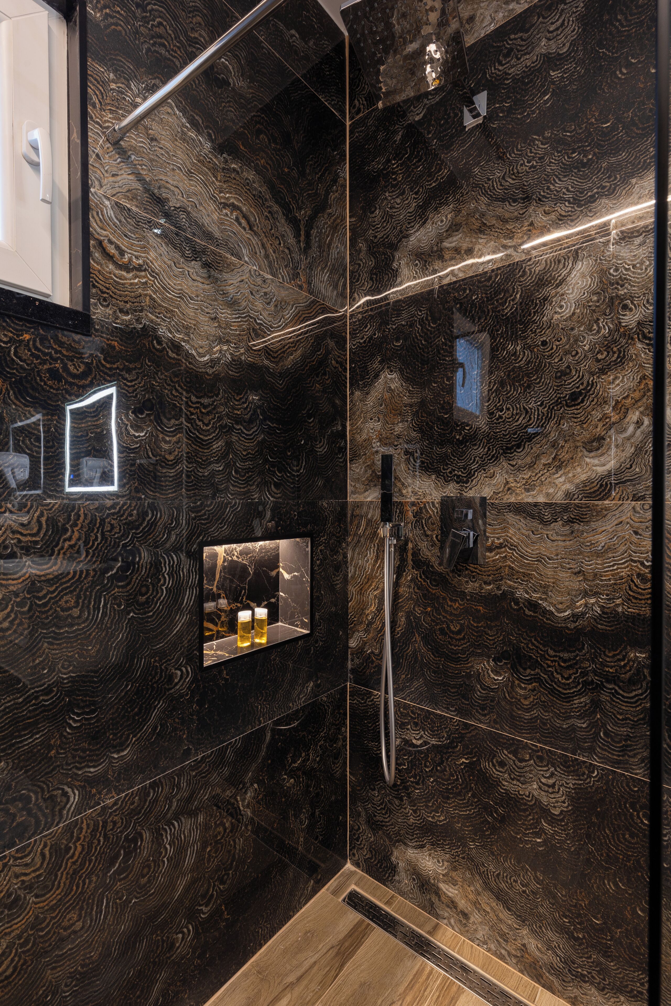 A bathroom with a marble wall, a shower, and a mirror with a framed picture.