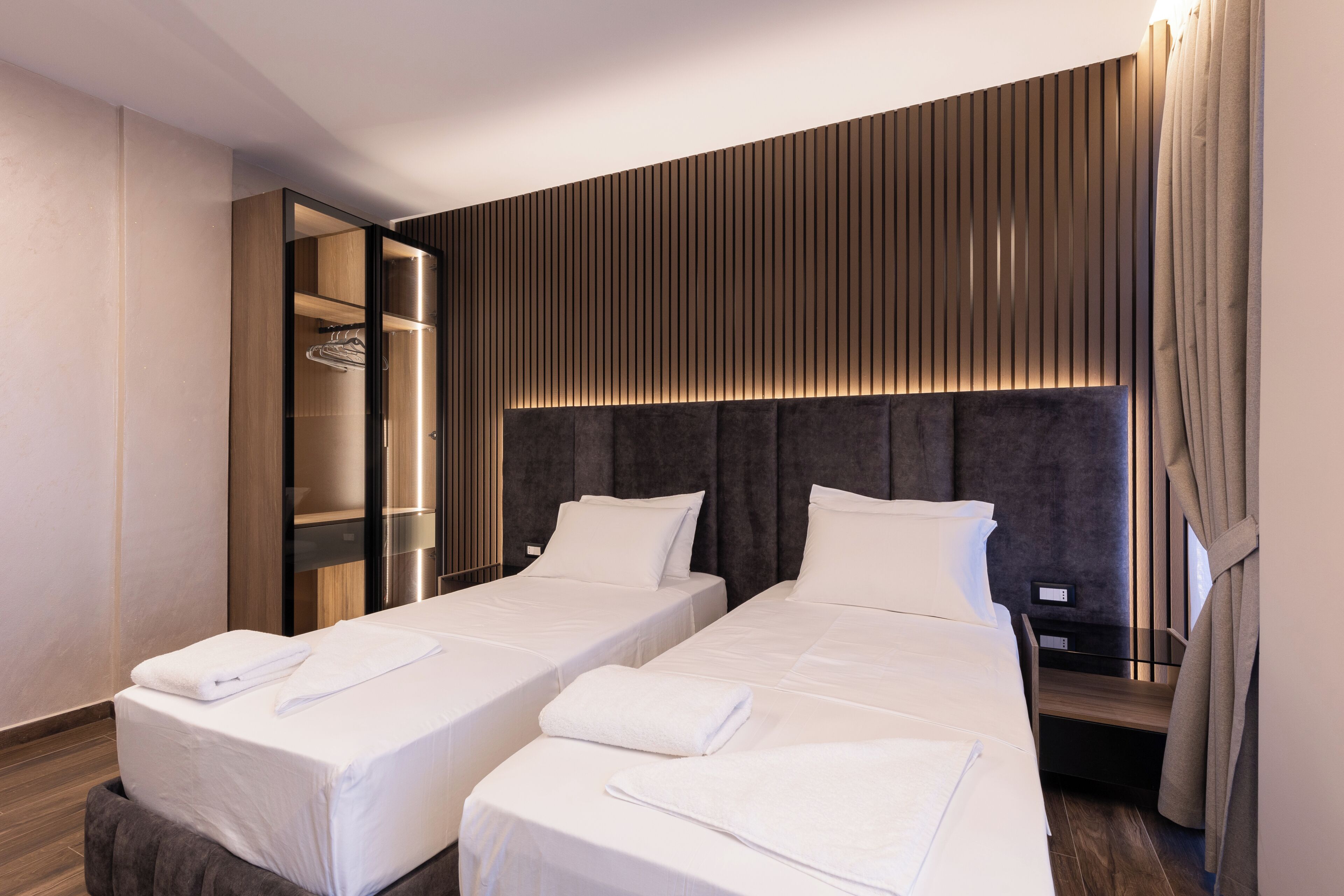 Una habitación de hotel con dos camas, un vestidor y un cabecero moderno.