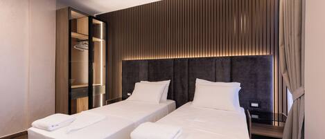 Una habitación de hotel con dos camas, un vestidor y un cabecero moderno.