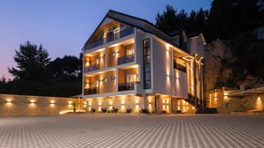 A modern multi-story building with balconies, stone walls, and a paved entrance area. - Forest Park Hotel Krujë (Fushe-Kruje)