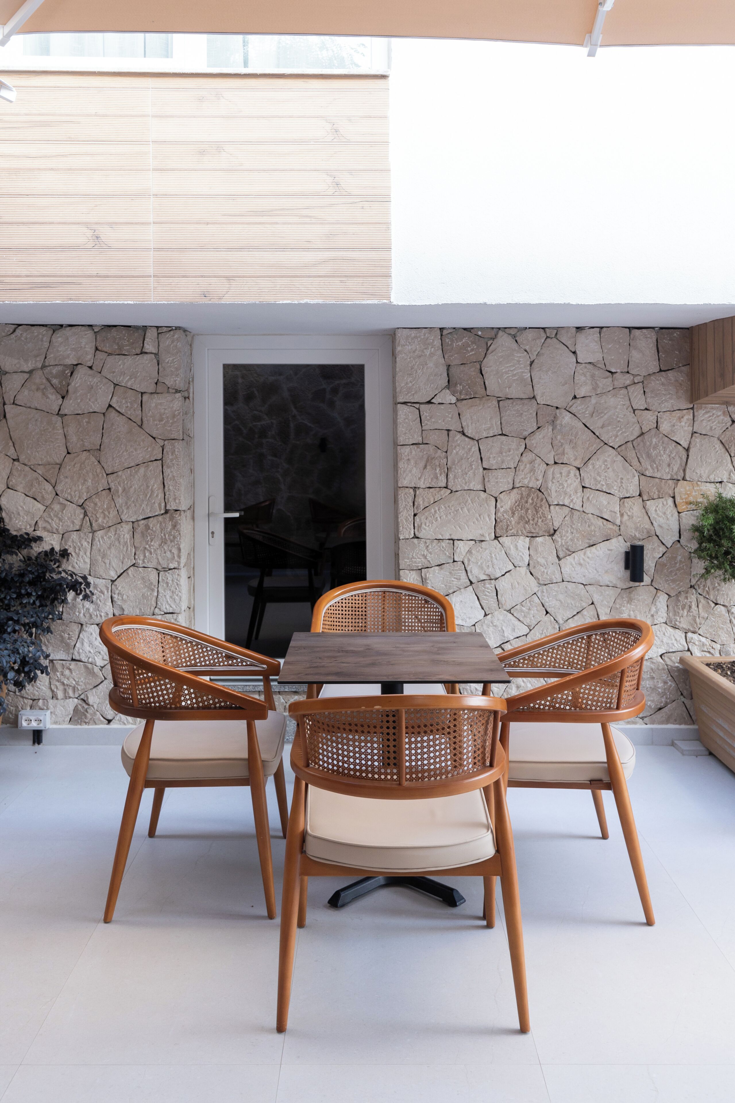 Un patio al aire libre con pared de piedra, mesa de madera y sillas de mimbre.