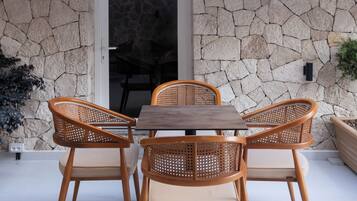 An outdoor patio with a stone wall, a wooden table, and wicker chairs.