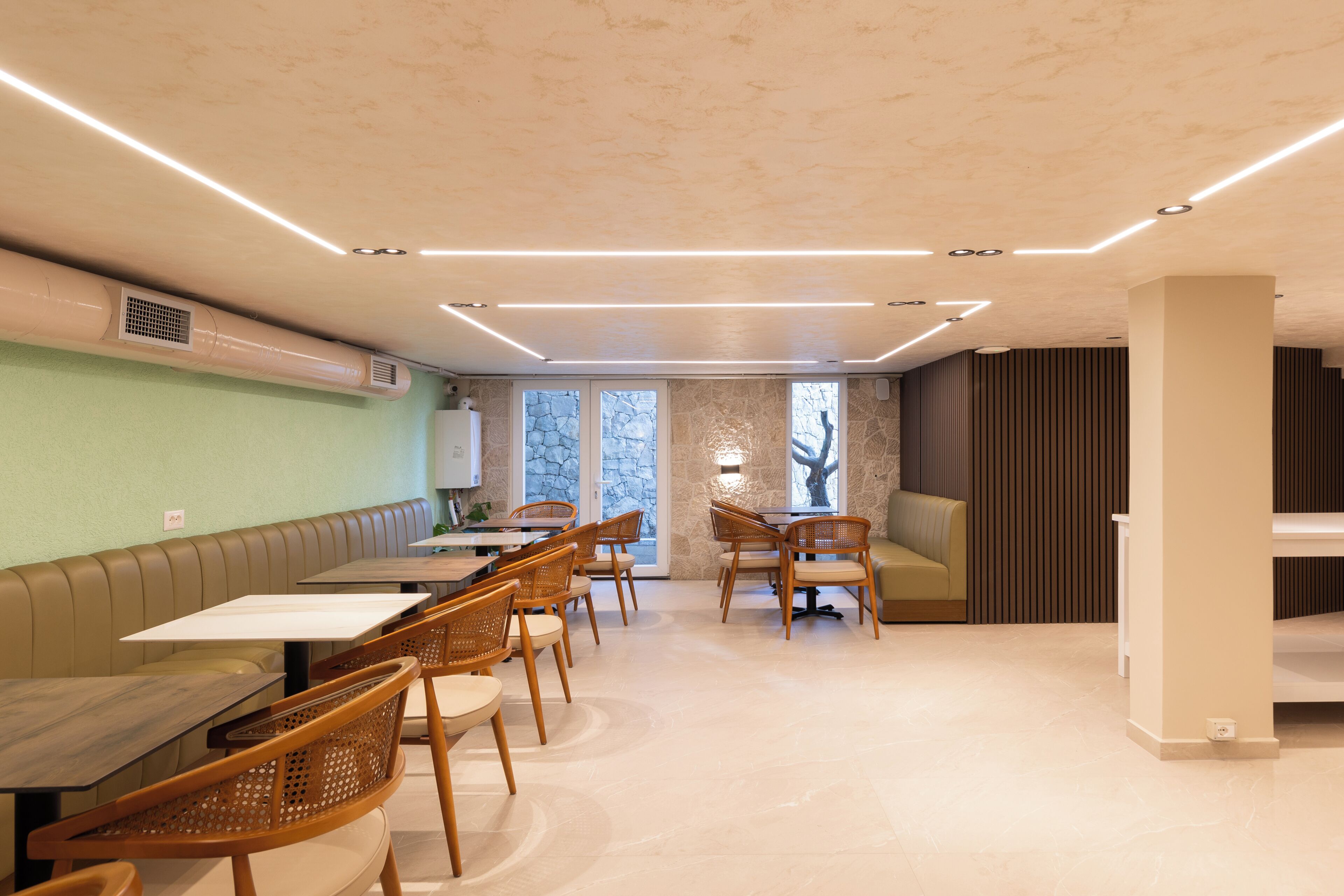 A modern dining area with tables and chairs, a bench, and a stone wall.
