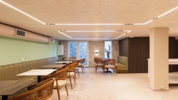 A modern dining area with tables and chairs, a bench, and a stone wall.