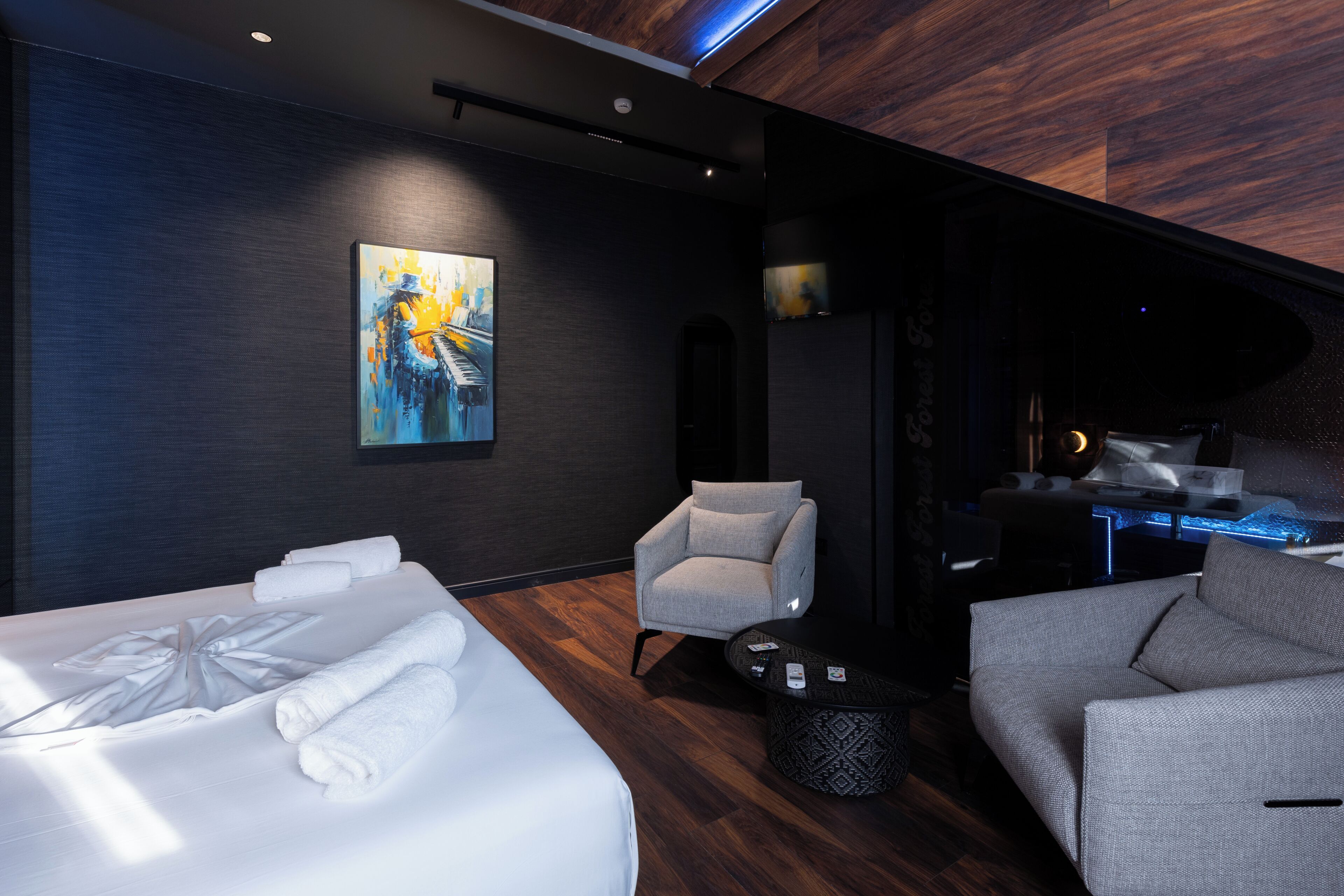 Ein modernes Hotelzimmer mit einem großen Bett, zwei Sesseln, einem kleinen Couchtisch und einem Bild an der Wand.