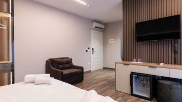 Ein modernes Hotelzimmer mit Bett, Sitzecke, Minibar und einem an einer Holzpaneelwand montierten Flachbildfernseher.