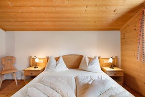 Una habitación con paneles de madera, una cama, dos mesitas de noche con lámparas, una silla de madera y un cortinaje decorado en una pared.