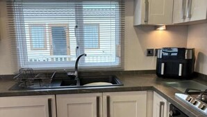 A modern kitchen with a built-in oven, a stainless steel sink, and a window with blinds. - Cabin Sleeps 4 With Beach Access & Parking (Lossiemouth)