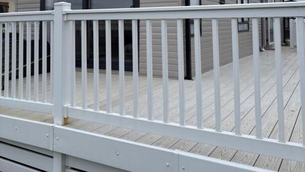 A modern, single-story building with a large glass window, a white deck, and a white railing. - Cabin Sleeps 4 With Beach Access & Parking (Lossiemouth)