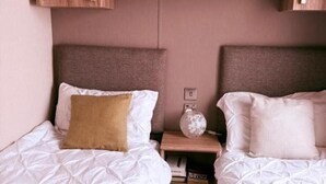 A room with two beds, a wooden shelf above, and a small table with a lamp. - Cabin Sleeps 4 With Beach Access & Parking (Lossiemouth)