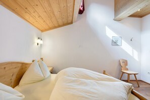 A bedroom with a wooden ceiling, a bed with white bedding, a wooden chair, and a wall-mounted light fixture. - Apartment Himmelschlüssel 19 with Mountain View and Wi-Fi (Santa Valburga)
