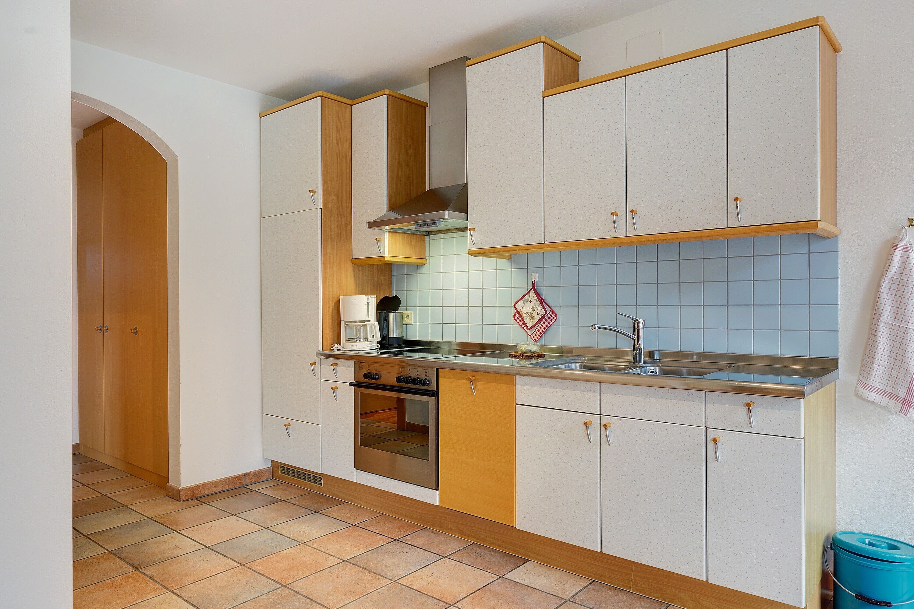 Eine Küche mit Holzausstattung, einer Spüle aus Edelstahl und einer gefliesten Rückwand.