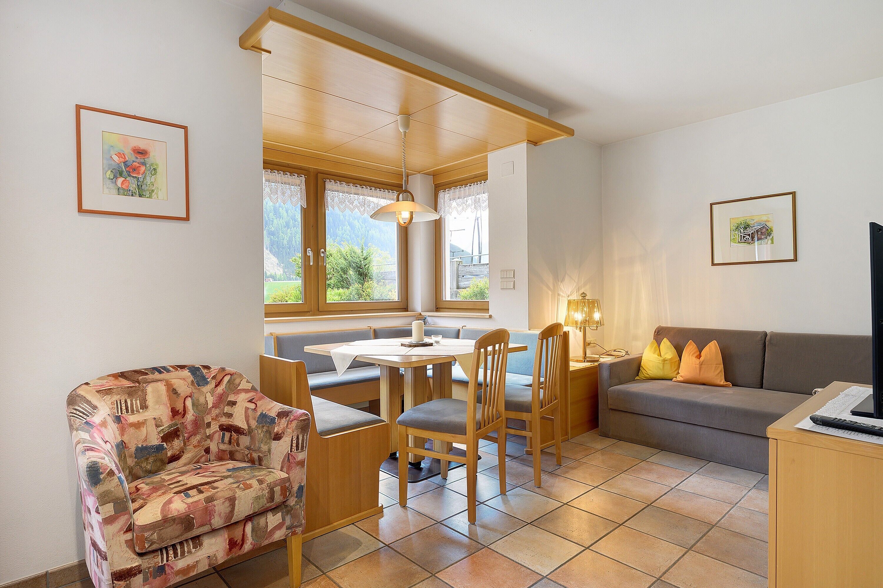 Ein Zimmer mit Esstisch, Stühlen, einer Couch, einem Fernseher und Bildern an den Wänden.