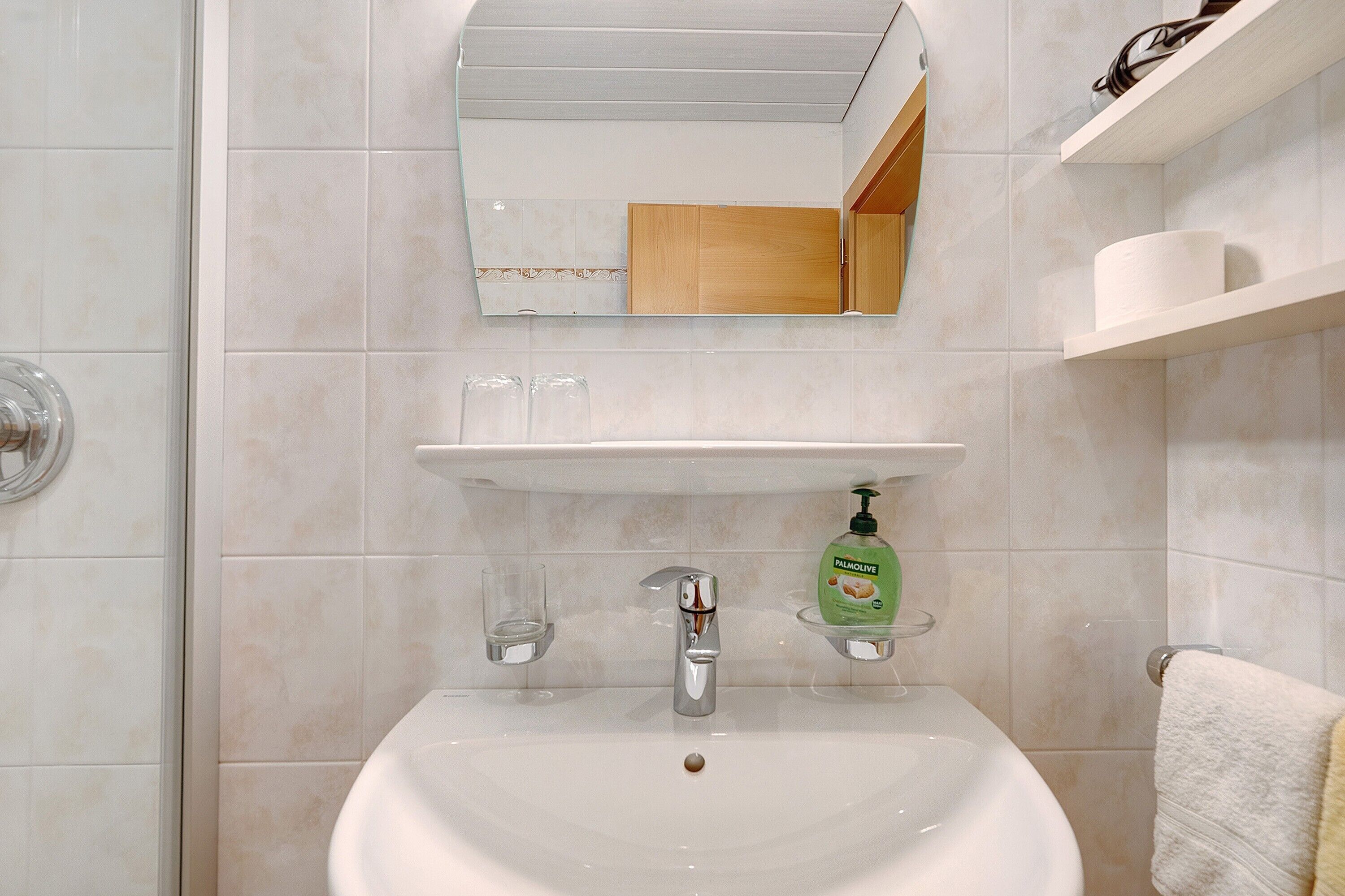 Un baño con lavamanos, espejo y estantes.