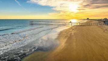 A beach with a wooden pier extending into the water, a clear sky, and a sunset.