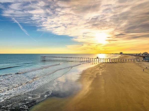 A beach with a wooden pier extending into the water, a clear sky, and a sunset.