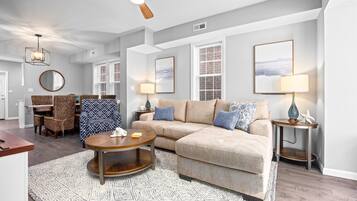 A modern living room with a sectional sofa, a round coffee table, and a dining area with wicker chairs.