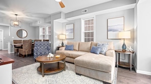 A modern living room with a sectional sofa, a round coffee table, and a dining area with wicker chairs.