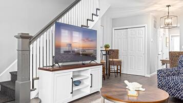 A living room with a TV on a wooden stand, a staircase, a door, and a patterned sofa.