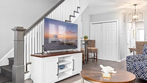 A living room with a TV on a wooden stand, a staircase, a door, and a patterned sofa.