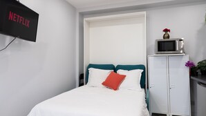 A bedroom with a bed, a TV mounted on the wall, a microwave on a cabinet, and a door leading to another room. - Apartment 'Calme  Elegant – Rer B – Paris' with Wi-Fi (Gentilly)