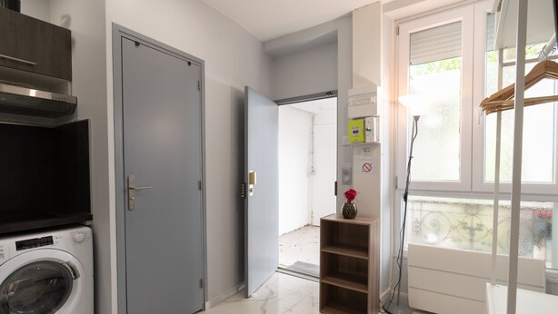 A laundry room with a washing machine, a gray door, and a window with a view. - Apartment 'Calme  Elegant – Rer B – Paris' with Wi-Fi (Gentilly)