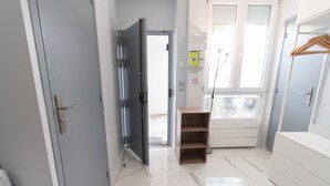 A hallway with a door, a wooden shelf, a white cabinet, and a window with blinds. - Apartment 'Calme  Elegant – Rer B – Paris' with Wi-Fi (Gentilly)