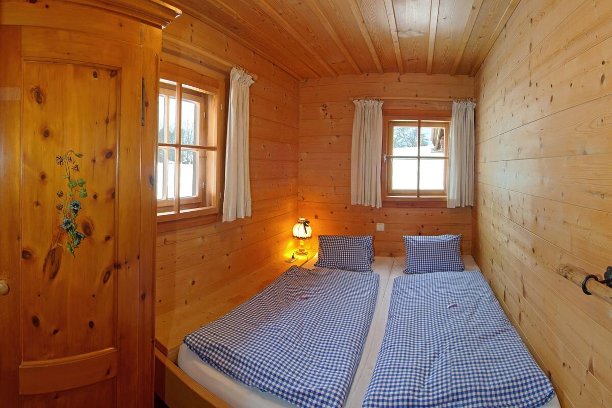 A wooden cabin room with two beds, a nightstand, and a window with curtains.