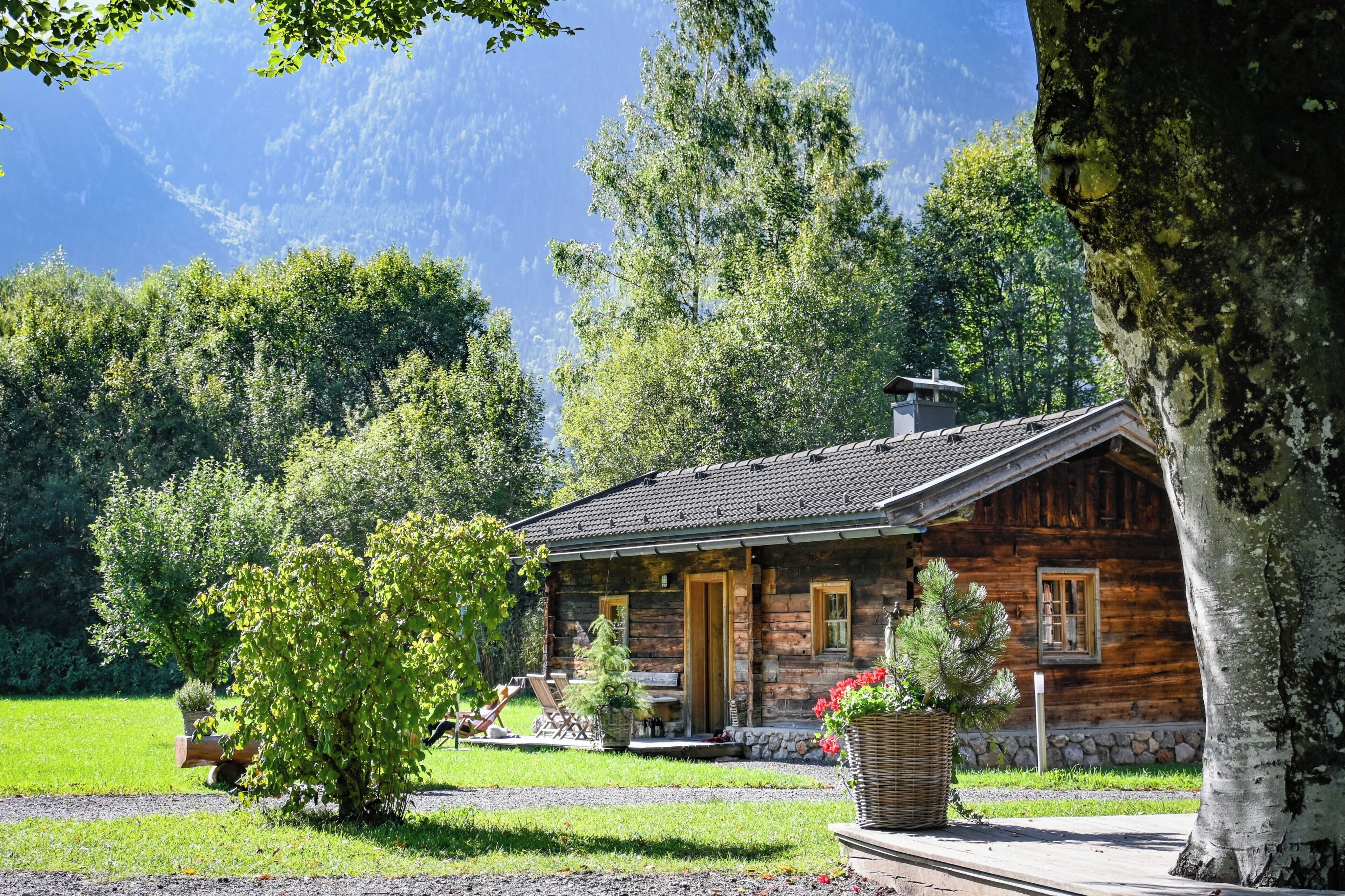 A rustic log cabin with a stone foundation, a chimney, and a porch with outdoor seating.