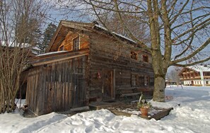 A rustic wooden cabin with a snow-covered roof, a wooden door, and a window.