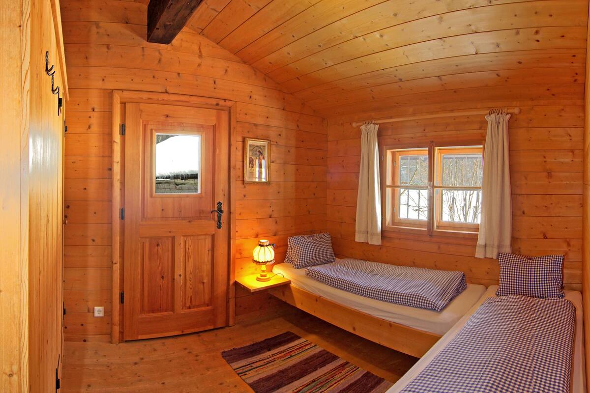 A wooden cabin room with a bed, bedside table, lamp, and a window.