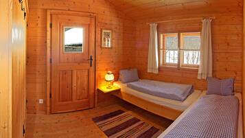 A wooden cabin room with a bed, bedside table, lamp, and a window.